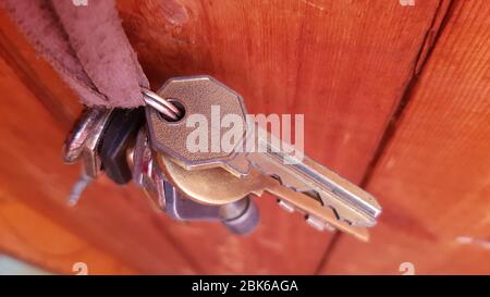 Retro keys in bunch hanging on dirty braid with wood background. Closeup of old metal keys of different sizes and shapes Stock Photo