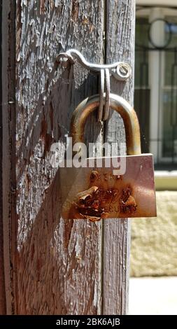 Old rusty padlock with shiny polished metal surface and flaking rust in bright sunlight and shadows. Vintage door lock closeup on blurry rough wooden Stock Photo