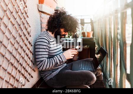 Young afro caucasian with laptop in his balcony Stock Photo