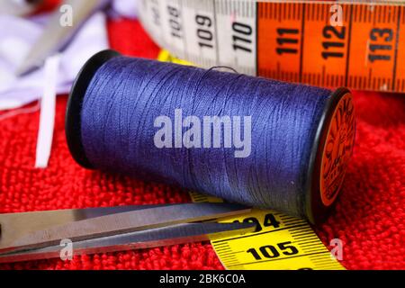 Viersen, Germany - April 30. 2020: Sewing work concept: Macro close up of isolated blue thread spool, scissors and measuring tape Stock Photo
