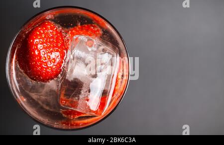Top view close up on isolated cocktail glass with red strawberries, sparkling tonic water and ice cubes (focus on ice cube right) Stock Photo