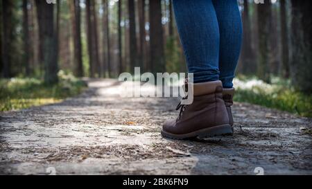 A man or a woman wearing brown hiking shoes walking on a wooden pathway with green grass and moss around the trail Stock Photo