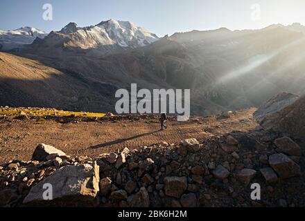 Hiker with backpack is walking on the road with spectacular mountains at background Stock Photo