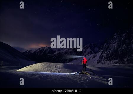 Man in red jacket with ray from his head light at starry night the mountain in ski resort at winter Stock Photo