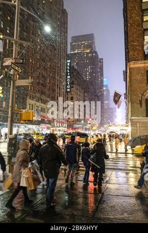 New York, NY/USA-December 2017: The corner of 7th Ave & W 56th St at night. Crowds of tourists and locals walking past during a snow storm Stock Photo