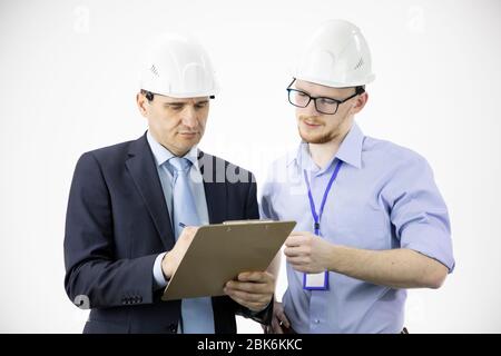 Engineer and architect in hard hats discuss project while making notes in clipboard Stock Photo