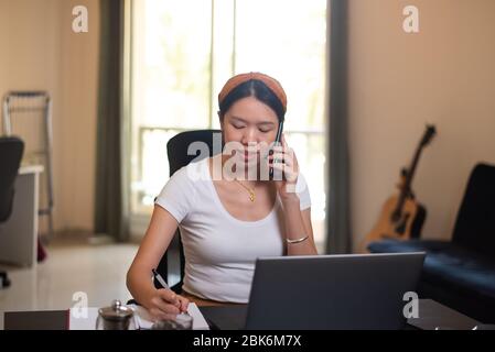 Busy woman on a phone meeting while working from home in an improvised office in the living room Stock Photo