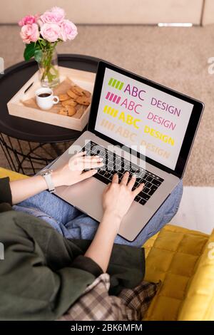 Hands of young female designer on laptop keypad during creative work in home environment by small table with snack, drink and roses Stock Photo