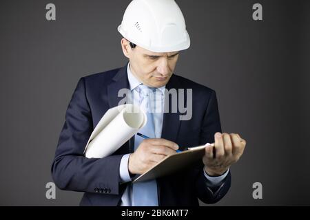 Chief engineer in safety helmet makes notes on clipboard holds blueprint roll Stock Photo