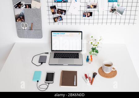 Home page of online shop on display of laptop on desk surrounded by notepad, smartphone, makeup products, drink and flowers Stock Photo