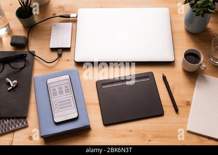 Mobile gadgets, pad with stylus, cup of coffee, notebooks, earphones, domestic plants and other stuff for work of modern designer Stock Photo