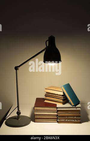 Light of lamp falling on pile of books or manuals of contemporary school or college student on desk in dark room at night Stock Photo