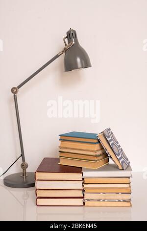 Lamp over stacks of books and manuals on table or workplace of student of college or school against white wall in studio Stock Photo