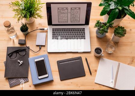 Flatlay of workplace of architect or designer with mobile gadgets, notebooks, eyeglasses, domestic plants, bottle of water and drinks Stock Photo