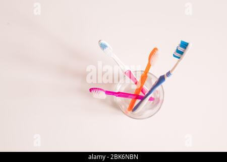 Overview of glass with bunch of new blue, orange and pink toothbrushes over white background with copyspace for notice on the left Stock Photo