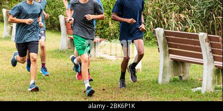 Four boys training for cross country racing together on the grass passing benches at a park. Stock Photo