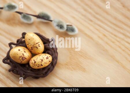 Chocolate nest, chocolate golden eggs and willow twig on light wooden background, copy space. Stock Photo