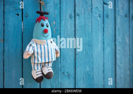 Faded soft doll in the shape of a blue man hangs on a blue wooden fence. Stock Photo