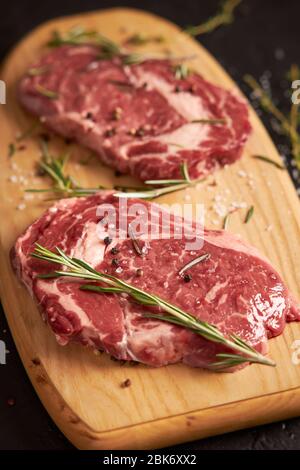 Two juicy slices of ribeye steak lie on a wooden board, vertical view. Stock Photo