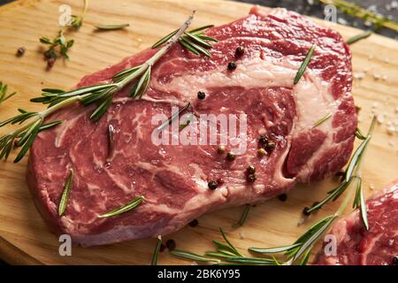 Raw fresh rib-eye steak with spices lies on a wooden board. Stock Photo