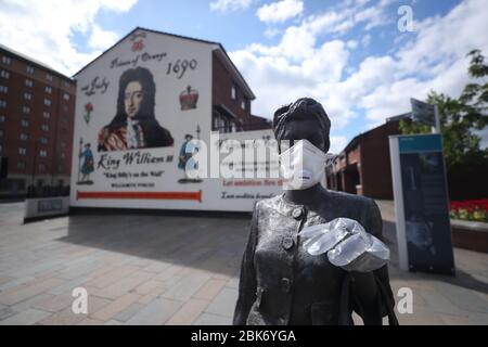 A statue by artist Ross Wilson entitled Mother Daughter Sister, celebrating female identity and culture, in Sandy Row Belfast is adorned with a mask and disposable gloves as the UK heads towards a seventh week in lockdown to try and limit the spread of coronavirus. Stock Photo