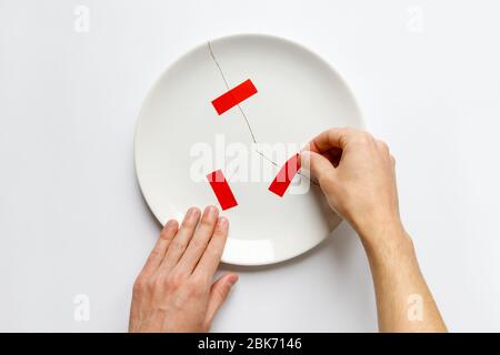 Top view of man hands holding a broken white plate, glues parts with red tape. Metaphor for divorce, relationships, friendships, crack in marriage. Is Stock Photo