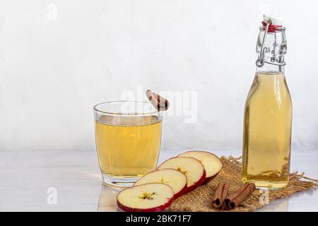 Healthy organic foods. Apple cider in a glass bowl and fresh red apples on a light background. In a glass of ice cubes and nearby cinnamon sticks. Cop Stock Photo