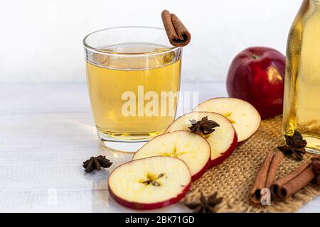 Healthy organic foods. Apple cider in a glass bowl and fresh red apples on a light background. In a glass of ice cubes and nearby cinnamon sticks. Cop Stock Photo