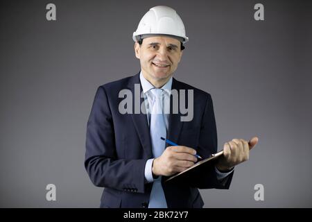 Oil engineer in hard hat makes notes on clipboard and looks at camera with smile Stock Photo