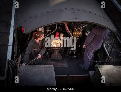 Bird's-eye view close up of steam train crew on footplate of vintage UK locomotive. Woman working in traditional man's job, role. Steam train driver. Stock Photo