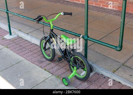 a close up view of a small kids green and black bicycle that has been locked to the railing to prevent it from being stolen while the owner is in the Stock Photo