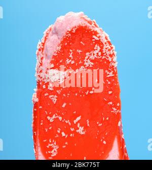 red popsicle with shredded coconut melting on a blue background Stock Photo