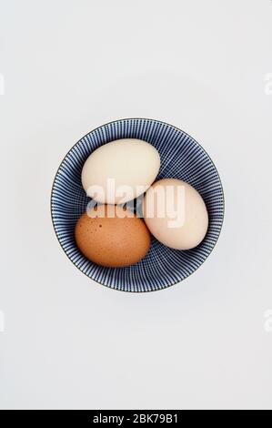 Three hens' eggs in small round Chinese bowl against white background Stock Photo