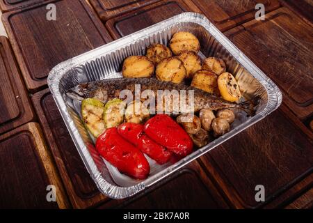 Appetizing mackerel fish baked on fire with spices, served on a plate and decorated with vegetables on wooden background Stock Photo