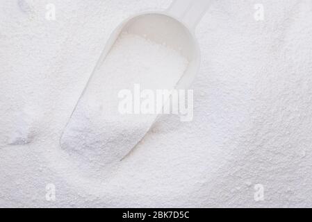 Close-up surface of white washing powder, washing laundry detergent powder in container with plastic scoop