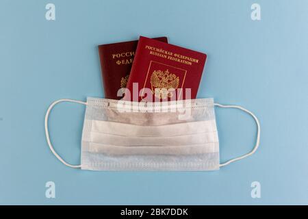 two Russian passports under a disposable medical mask on a blue background close-up view from above, the concept of self-isolation during the coronavi Stock Photo