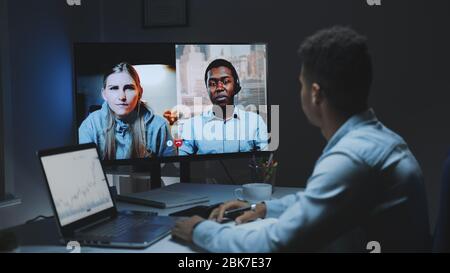 Mixed-race colleagues working home on quarantine by making common video call on a big monitor. They working late at night. Stock Photo