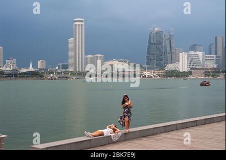 26.08.2019, Singapore, Republic of Singapore, Asia - Thunderstorm atmosphere over Marina bay with two young women at the waterfront. Stock Photo