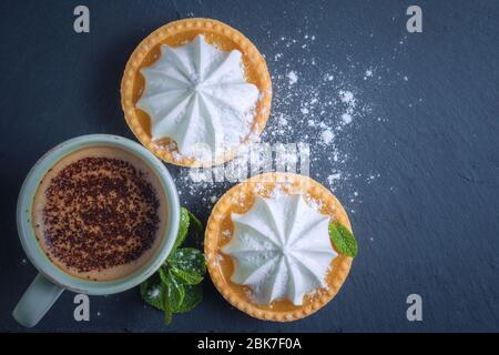 Lemon tart with mint leaves and a cup of cappuccino with chocolate topping. View from above Stock Photo