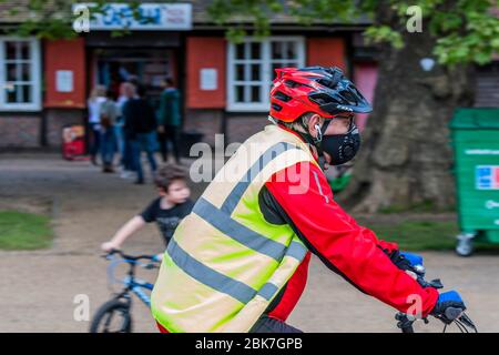 London, UK. 02nd May, 2020. A man in a mask cycles past the entrance - The cafe near the closed bandstand is now open, for drinks and ice cream, with a one way system and social distancing. Clapham Common is reasonably busy as the sun is out and it is warmer. The 'lockdown' continues for the Coronavirus (Covid 19) outbreak in London. Credit: Guy Bell/Alamy Live News Stock Photo