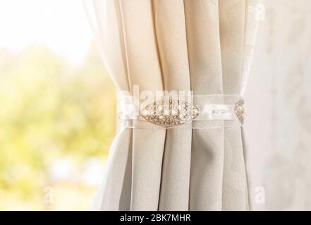Close up view of curtain holder indoors, home decor. Minimalist gray curtain in white bedroom with sun lens flare. Stock Photo