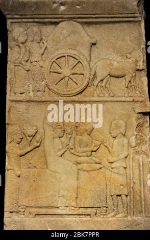 Anatolian-Persian funerary stele, 5th century BC. Marble.From Daskylaion (Ergili, Lake Manyas). Detail of the upper part of the stele depicting a funerary cortege in two scenes: two mourning women walk behind a funeral cart (upper scene). A woman and a bearded man sit on a couch (lower scene). The woman's left hand holds an object, while her right hand receives an egg from the man. The couch is flanked by servants or slaves. On the right, the slave stands in front of a vessel placed on a tripod. On the left, the other slave carries a fruit bowl. Archaeological Museum. Istanbul, Turkey. Stock Photo