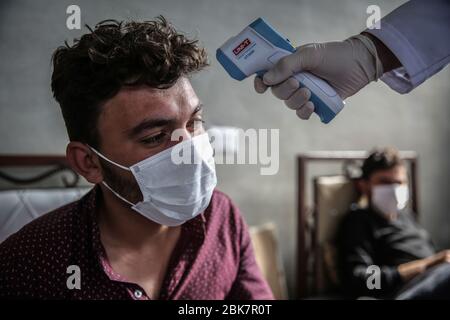 Jisr Al Shughur, Syria. 02nd May, 2020. A medic checks the temperature of a man inside a health isolation centre which has been established on the Syrian-Turkish borders in order to place people coming from Turkey to Idlib as a preventive measure against the spread of the coronavirus disease (COVID-19). The centre is supervised by a medical team trained in all measures to be taken to deal with expats as the centre has received more than 600 people so far and the isolation period is 15 days. Credit: Anas Alkharboutli/dpa/Alamy Live News Stock Photo
