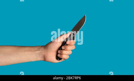 Closeup of young guy holding pocket knife on blue background, blank space. Panorama Stock Photo