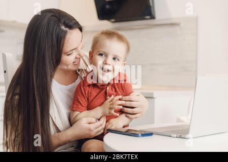 Business mom is using online work laptop, woman spending time with her boy baby home Stock Photo