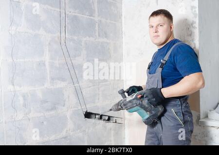 Builder worker man using jackhammer to drill into construction wall for duct for air conditioning pipes Stock Photo