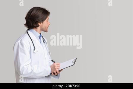 Confident doctor writing notes on clipboard and looking at copy space Stock Photo