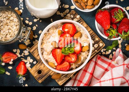 Oatmeal porridge with fresh strawberry and nuts on dark background. Stock Photo