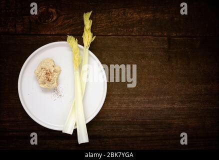 Fresh stick celery with hummus on wooden table Stock Photo