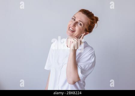 Nice young girl redhead with headphones laughing looking at camera over white background. Stock Photo